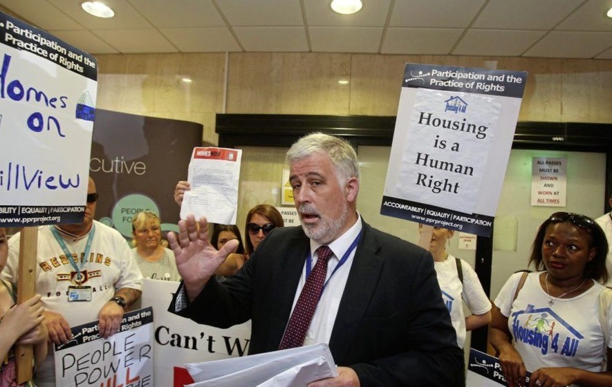 Housing Executive boss stands in the middle of an impromptu protest in his building surrounded by protestors with placards 