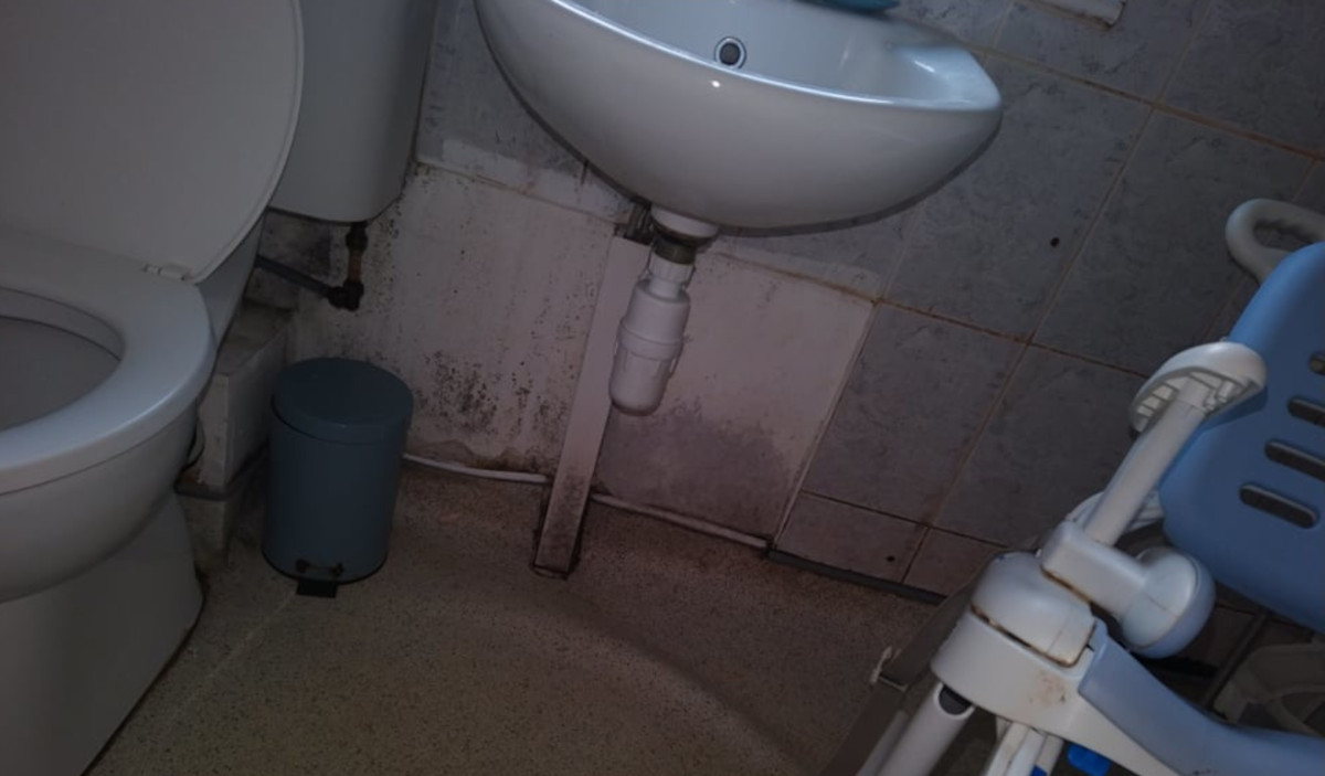 Picture of a toilet, washing basin and an chair aid with damp and mould on the bathroom walls