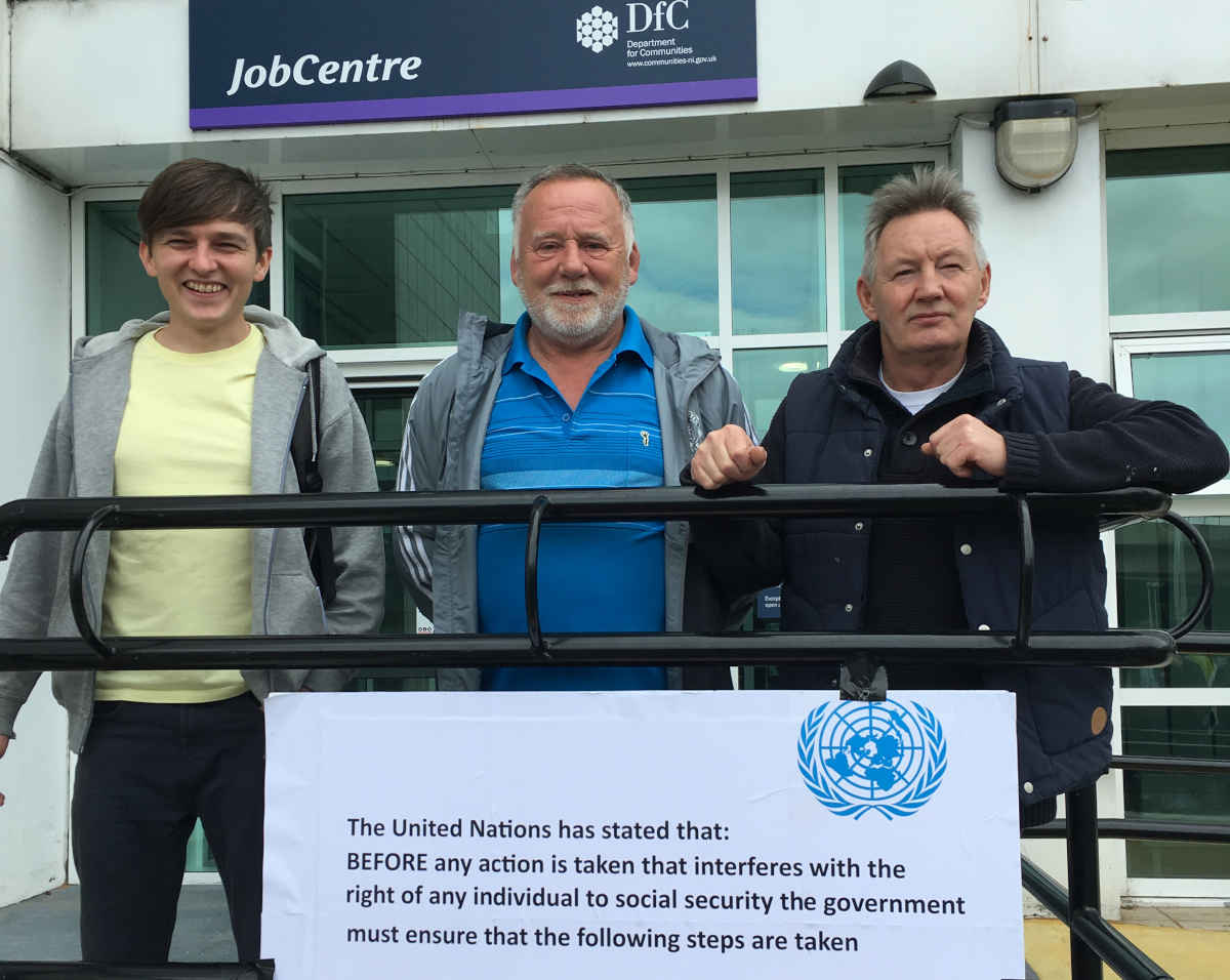 Three man stand in front of a government building with railings and a placard with the United Nations logo 